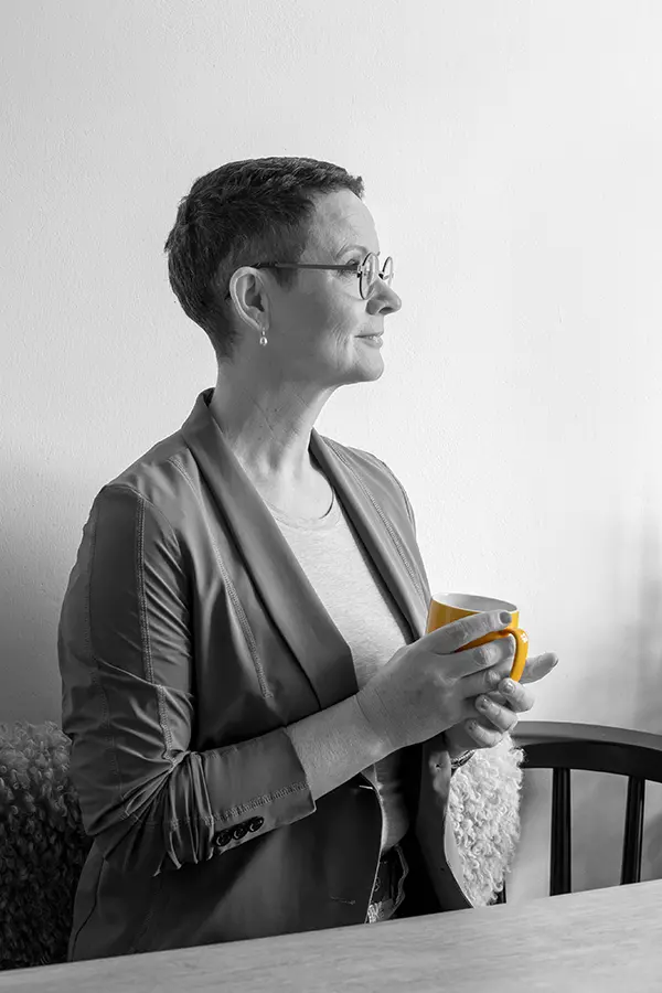 Imke Koop, Gründerin von KMU Voice und zertifizierte Voice Consultant, sitzt im Profil hinter einem Tisch und hält eine Tasse Tee in der Hand. Das Foto ist in schwarz-weiß, lediglich die Tasse ist in Farbe - einem leuchtenden Gelb.